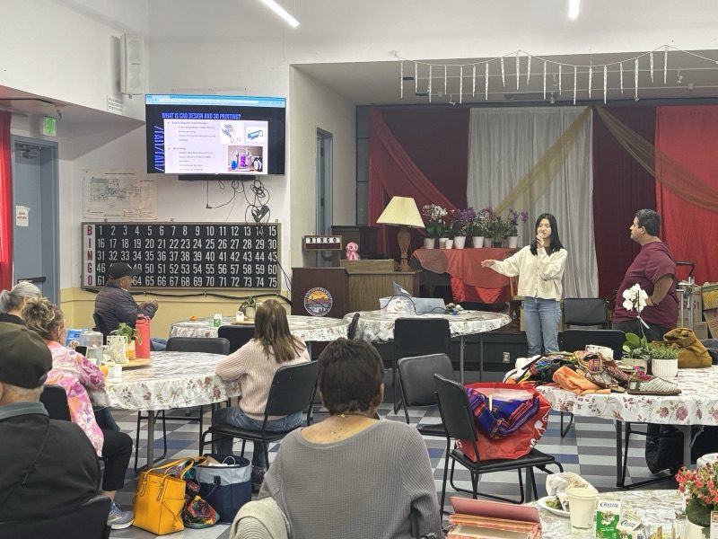 Yanzi presenting at the front of a large hall with residents seated at round tables