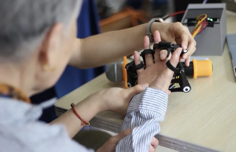Hands guiding an older person's fingers into the exoskeleton's fingertip clips