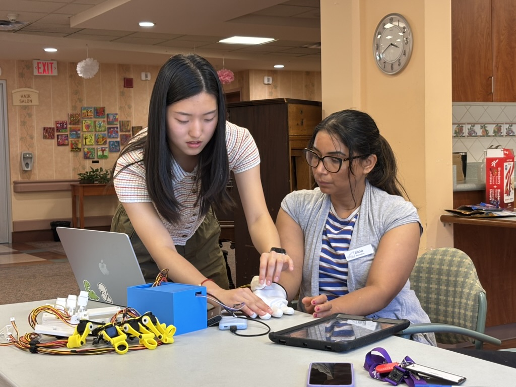Angela guiding a participant through a Ripple sensor-glove demonstration at a senior center